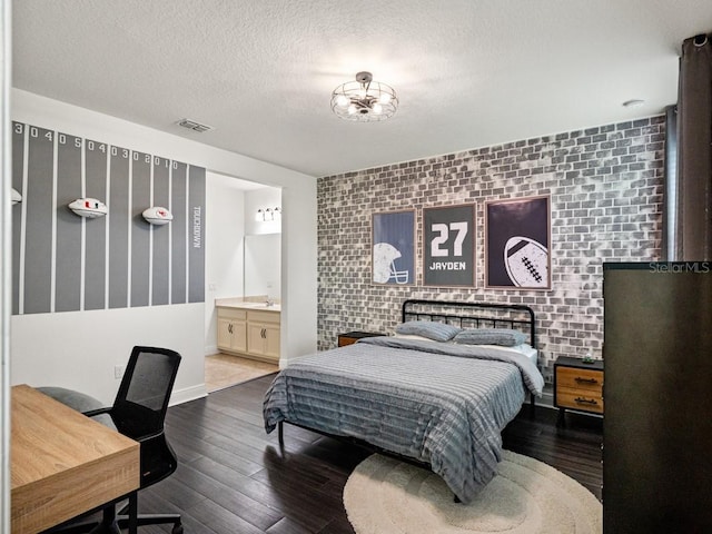 bedroom with hardwood / wood-style flooring, a textured ceiling, brick wall, and ensuite bath