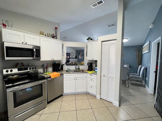 kitchen with lofted ceiling, sink, light tile patterned floors, white cabinetry, and stainless steel appliances