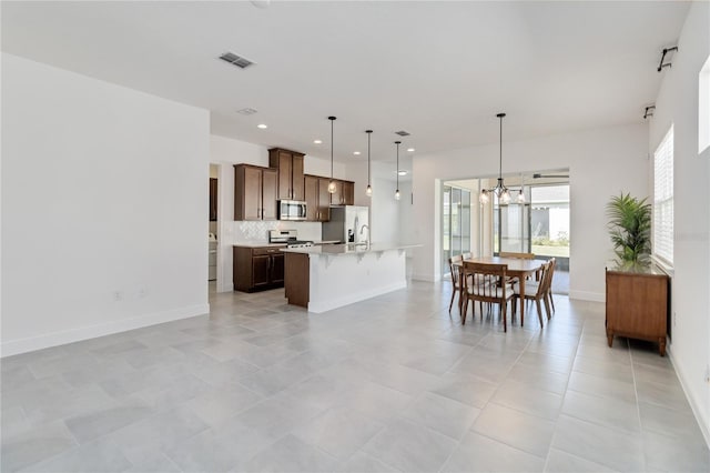 kitchen with pendant lighting, a center island with sink, appliances with stainless steel finishes, tasteful backsplash, and a notable chandelier