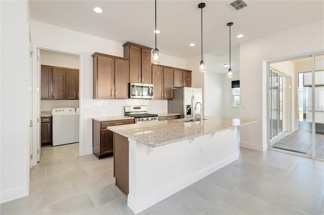 kitchen with appliances with stainless steel finishes, washer / clothes dryer, hanging light fixtures, and an island with sink