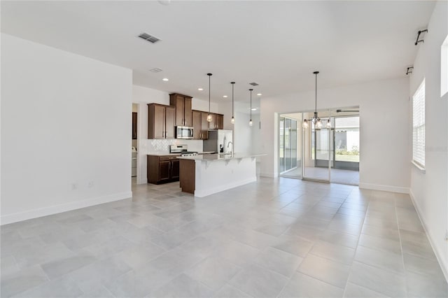 kitchen with appliances with stainless steel finishes, backsplash, a notable chandelier, hanging light fixtures, and an island with sink