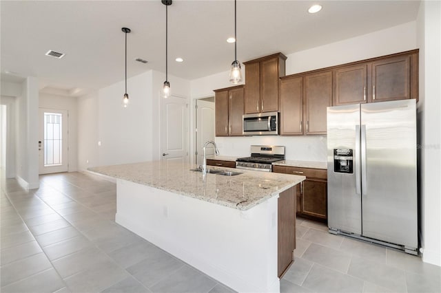 kitchen featuring a kitchen island with sink, sink, stainless steel appliances, and decorative light fixtures