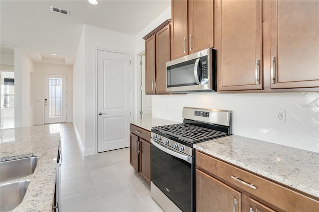 kitchen with decorative backsplash, light tile patterned flooring, light stone counters, and stainless steel appliances