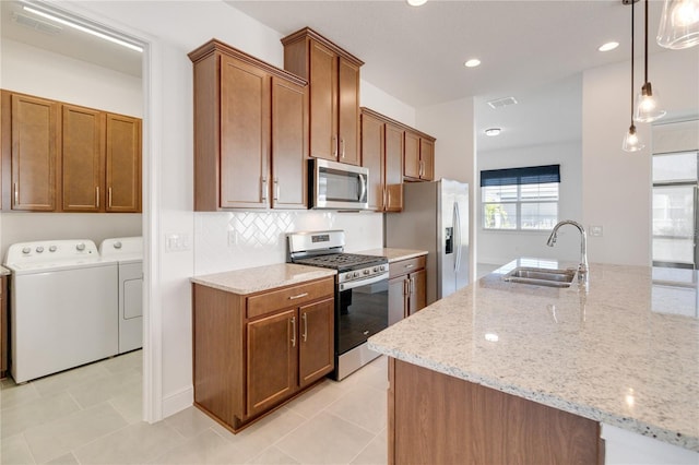 kitchen featuring sink, light stone countertops, separate washer and dryer, appliances with stainless steel finishes, and decorative light fixtures