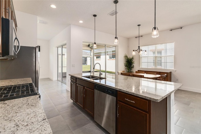 kitchen with appliances with stainless steel finishes, light stone counters, a kitchen island with sink, sink, and pendant lighting