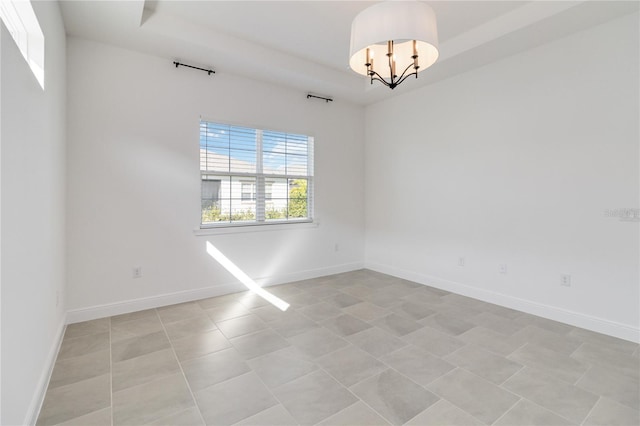 empty room with a raised ceiling and an inviting chandelier