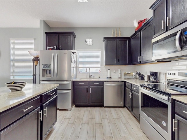 kitchen with appliances with stainless steel finishes, light stone countertops, sink, and dark brown cabinets