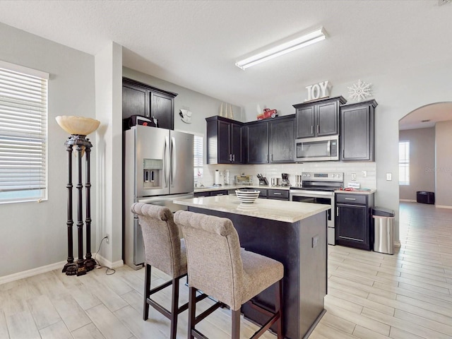 kitchen featuring tasteful backsplash, light wood-type flooring, a kitchen breakfast bar, a kitchen island, and stainless steel appliances