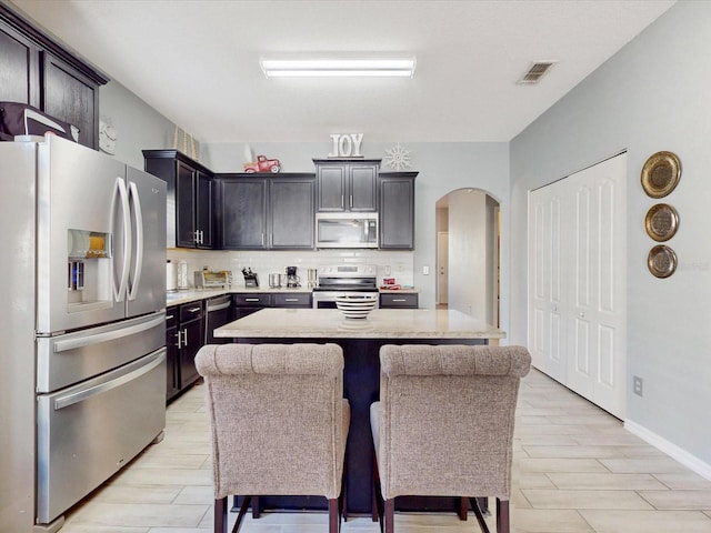 kitchen featuring tasteful backsplash, a kitchen bar, a kitchen island, and appliances with stainless steel finishes