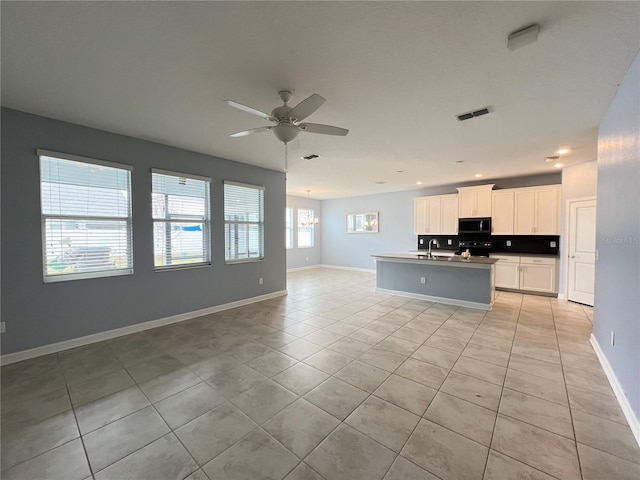 kitchen featuring ceiling fan with notable chandelier, sink, an island with sink, light tile patterned flooring, and white cabinetry