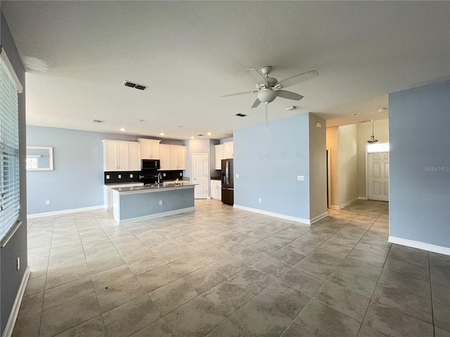 kitchen featuring stainless steel fridge, ceiling fan, sink, white cabinets, and an island with sink