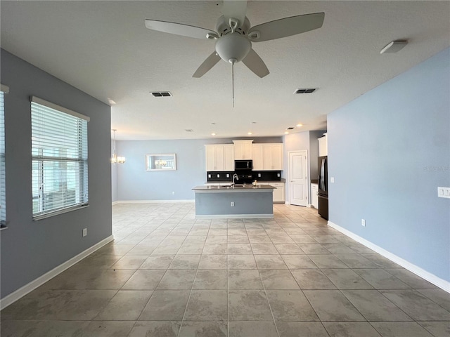 kitchen featuring stainless steel fridge, ceiling fan with notable chandelier, a center island with sink, white cabinets, and light tile patterned flooring