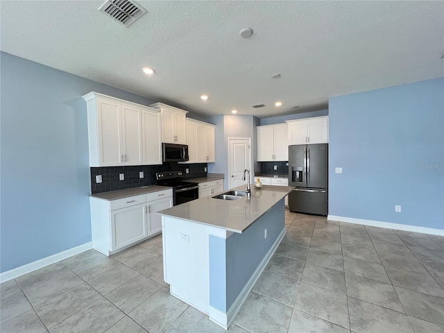 kitchen with appliances with stainless steel finishes, sink, light tile patterned floors, white cabinetry, and an island with sink