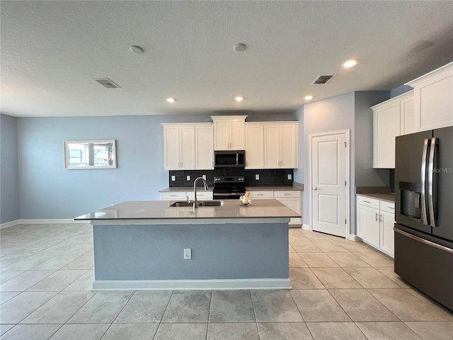 kitchen with appliances with stainless steel finishes, a kitchen island with sink, sink, white cabinets, and light tile patterned flooring