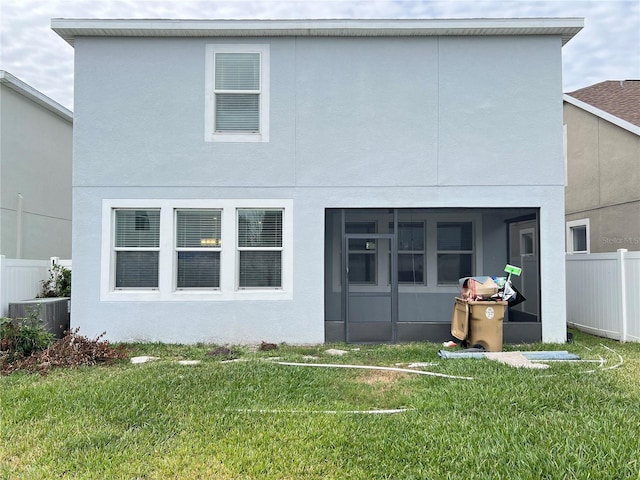 rear view of house with central AC unit, a sunroom, and a lawn