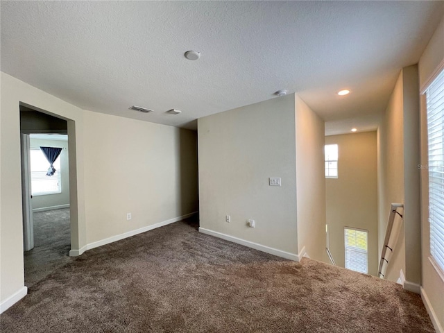 spare room with a textured ceiling, dark carpet, and a wealth of natural light