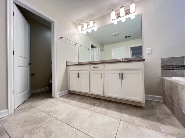 bathroom with vanity, a textured ceiling, tiled tub, tile patterned flooring, and toilet