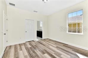 unfurnished bedroom with ensuite bathroom and light hardwood / wood-style flooring