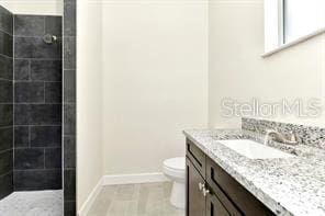 bathroom with tiled shower, vanity, and toilet