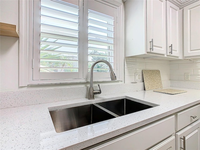 kitchen with backsplash, white cabinetry, sink, and light stone counters