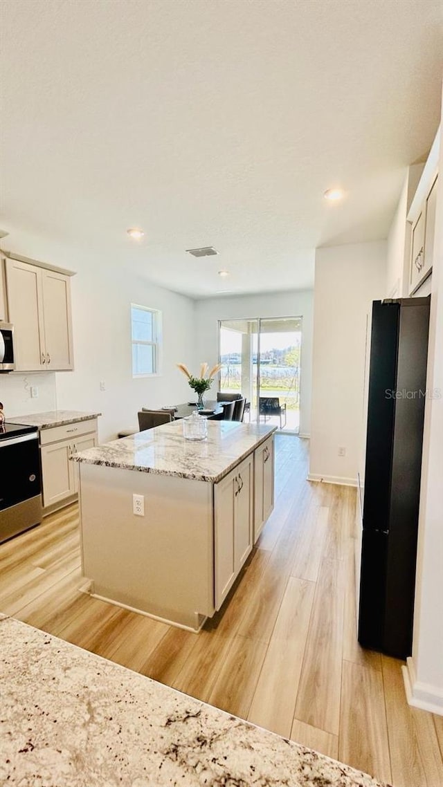 kitchen with light stone counters, a kitchen island, light hardwood / wood-style floors, and appliances with stainless steel finishes