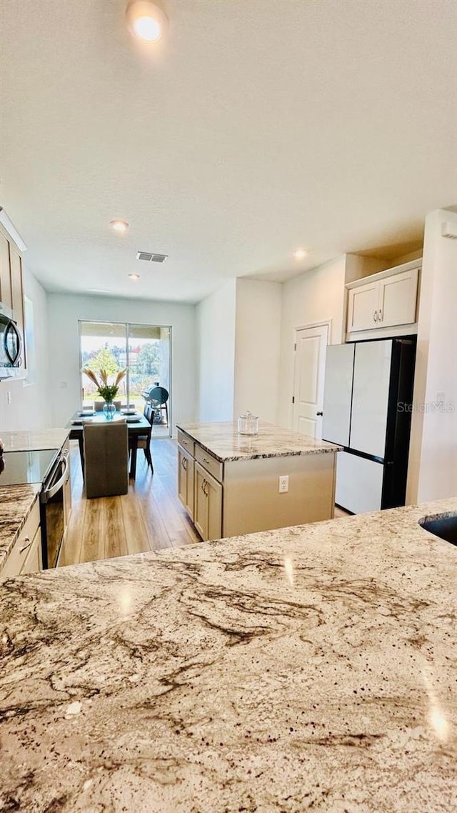 kitchen featuring stainless steel electric range oven, a center island, light stone countertops, white fridge, and light wood-type flooring