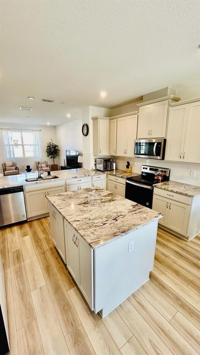 kitchen with light stone counters, kitchen peninsula, light wood-type flooring, and appliances with stainless steel finishes