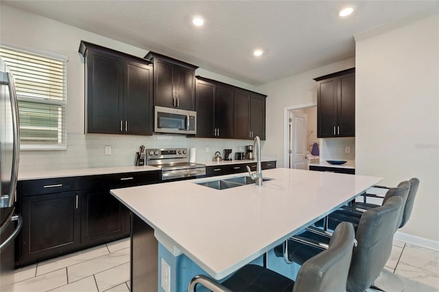 kitchen with a kitchen breakfast bar, backsplash, stainless steel appliances, a kitchen island with sink, and sink