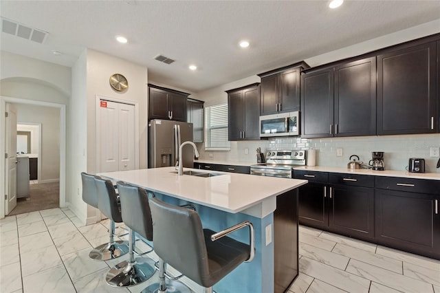 kitchen featuring backsplash, stainless steel appliances, sink, a breakfast bar area, and an island with sink