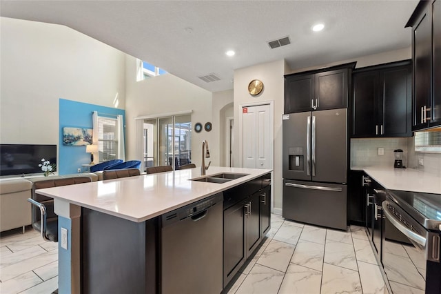 kitchen with sink, stainless steel appliances, a kitchen island with sink, and tasteful backsplash