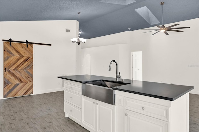 kitchen featuring lofted ceiling with skylight, ceiling fan with notable chandelier, sink, a barn door, and white cabinetry