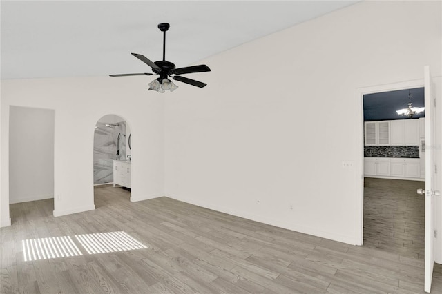 spare room featuring ceiling fan with notable chandelier, light hardwood / wood-style flooring, and vaulted ceiling