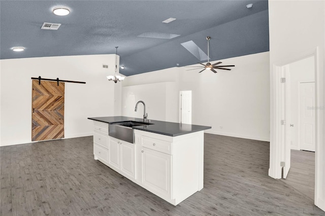 kitchen featuring vaulted ceiling, sink, pendant lighting, a barn door, and white cabinets