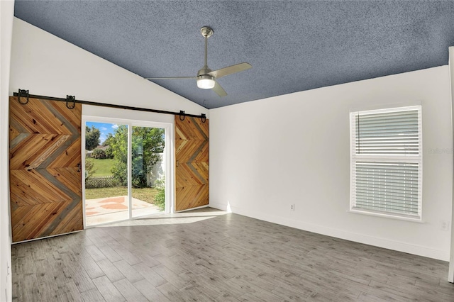 interior space featuring hardwood / wood-style flooring, ceiling fan, a barn door, and vaulted ceiling