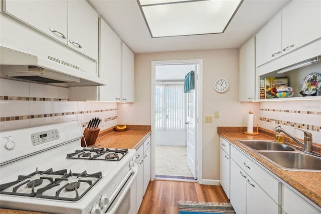 kitchen featuring sink, light wood-type flooring, white range with gas cooktop, decorative backsplash, and white cabinets