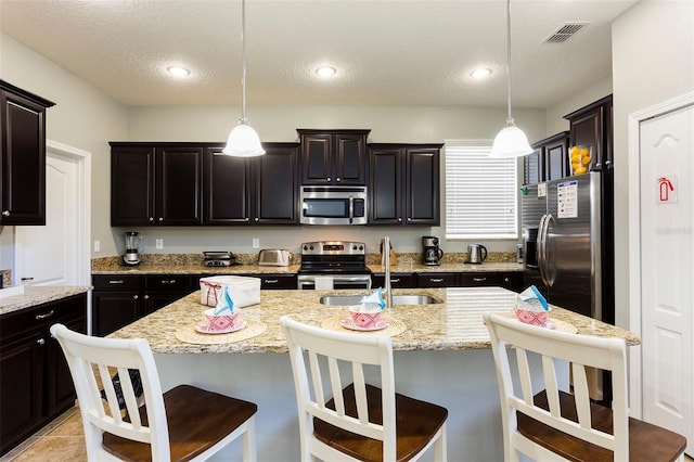 kitchen featuring decorative light fixtures, an island with sink, stainless steel appliances, and sink