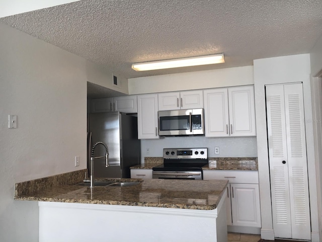 kitchen featuring white cabinets, kitchen peninsula, stainless steel appliances, and a textured ceiling