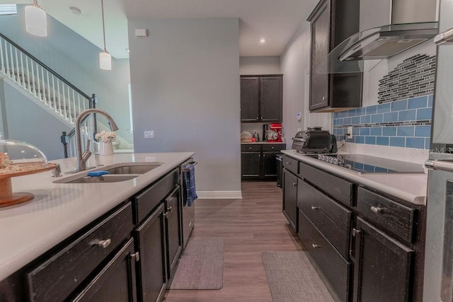 kitchen featuring pendant lighting, wall chimney range hood, black electric stovetop, sink, and light wood-type flooring