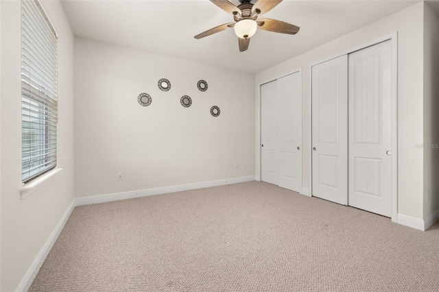 unfurnished bedroom with ceiling fan, light carpet, and multiple closets