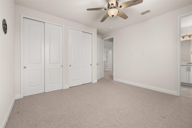 unfurnished bedroom featuring ceiling fan, ensuite bathroom, light carpet, and multiple closets