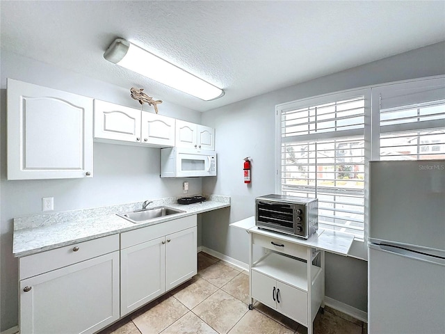 kitchen with white cabinetry, sink, refrigerator, a textured ceiling, and light tile patterned flooring