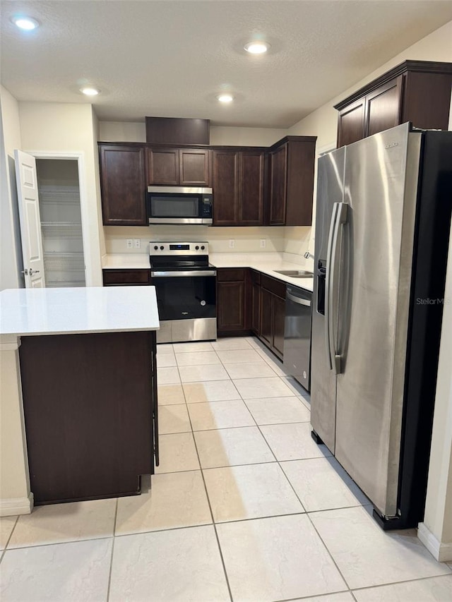 kitchen with dark brown cabinetry, light tile patterned floors, and appliances with stainless steel finishes