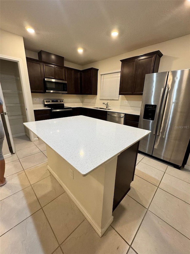 kitchen featuring sink, a kitchen island, light tile patterned floors, and appliances with stainless steel finishes