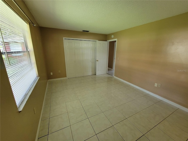 unfurnished bedroom with light tile patterned floors, a textured ceiling, and a closet