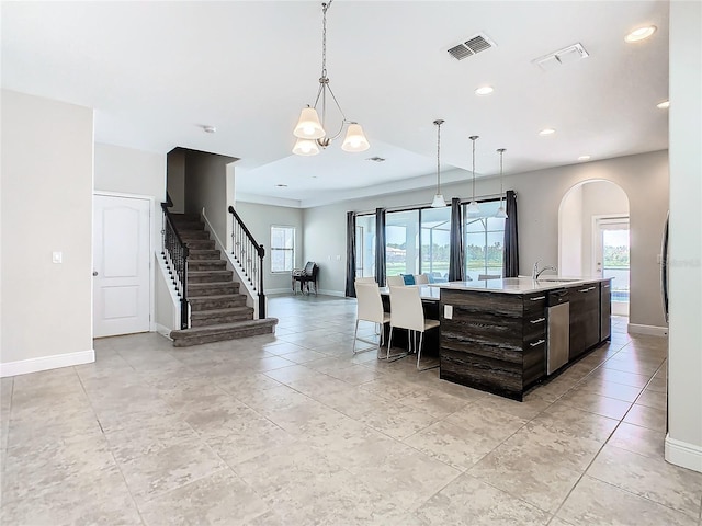 kitchen with hanging light fixtures, an inviting chandelier, stainless steel dishwasher, a center island with sink, and dark brown cabinets