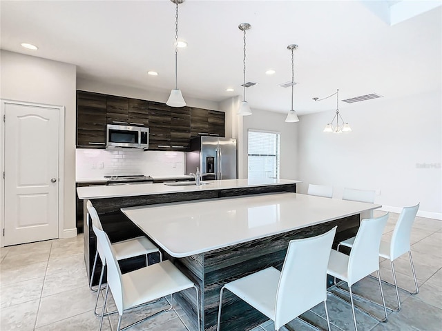 kitchen with sink, hanging light fixtures, backsplash, an island with sink, and appliances with stainless steel finishes