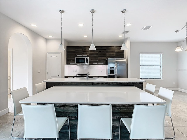 kitchen with tasteful backsplash, appliances with stainless steel finishes, a center island with sink, and decorative light fixtures