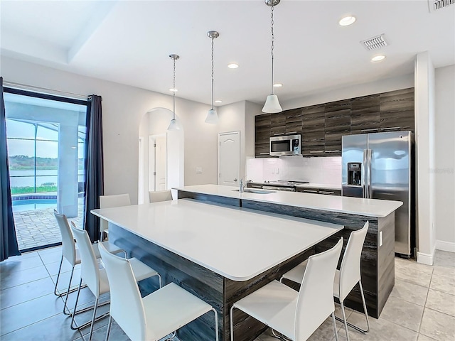 kitchen with a breakfast bar, a center island with sink, decorative light fixtures, and appliances with stainless steel finishes