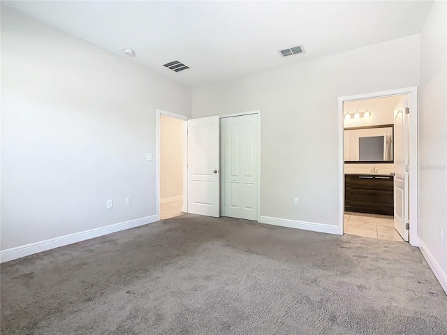 unfurnished bedroom featuring ensuite bath, light carpet, and a closet