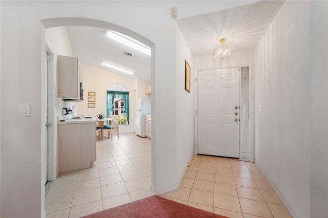 entryway with a textured ceiling, an inviting chandelier, vaulted ceiling, and light tile patterned flooring